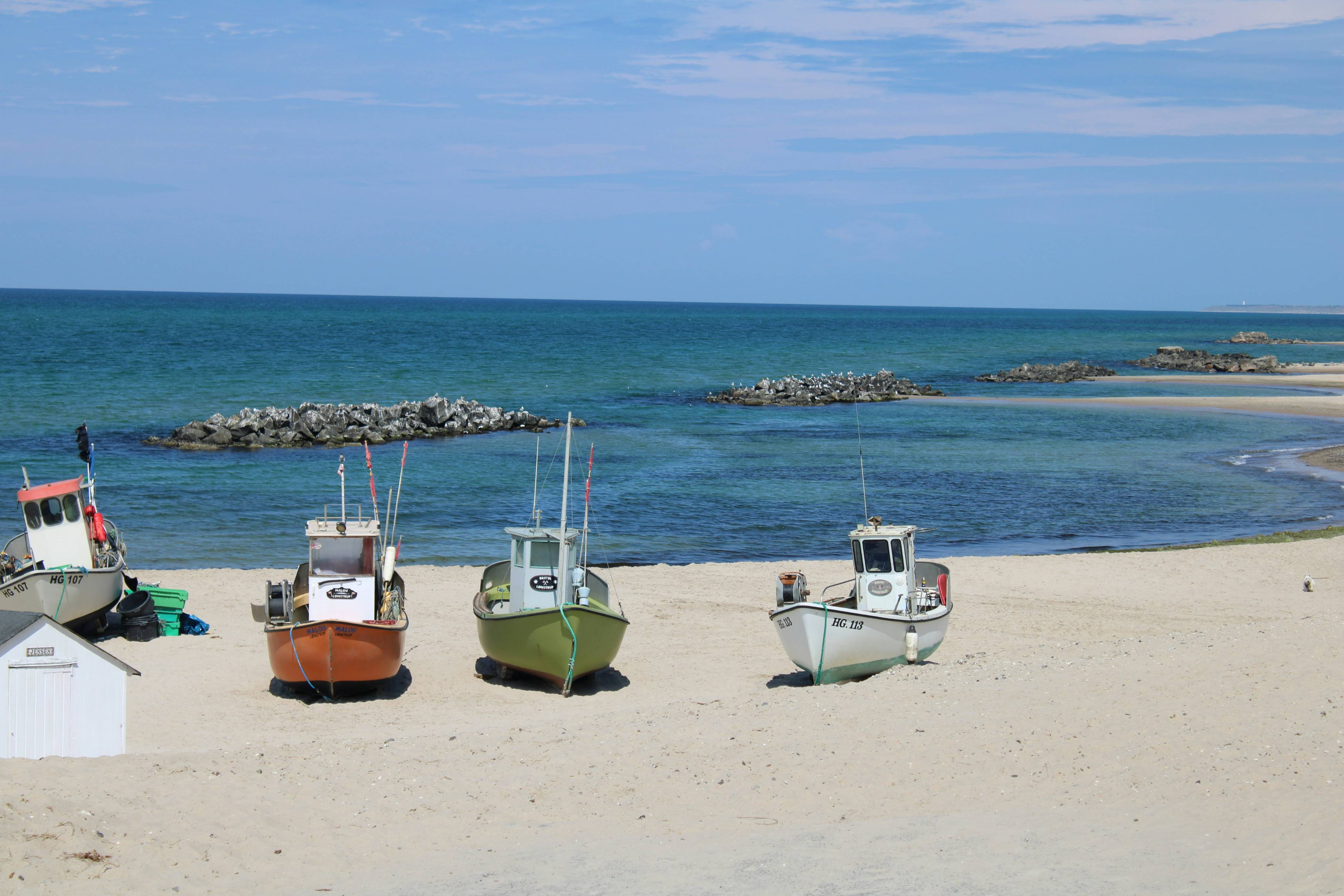 Fishing boats rest on a sandy beach by the ocean.
